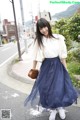 A woman in a white shirt and blue skirt is walking down the street.