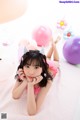 A young girl laying on a pink rug surrounded by balloons.