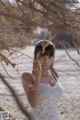 A woman in a white dress standing under a tree.