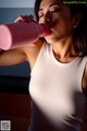 A woman in a white tank top drinking from a pink bottle.